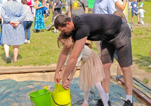 Dzieci z Rodzicami korzystają z okazji robienia dużych baniek mydlanych.