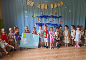 Dzieci prezentują swoją pracę na tle letniej dekoracji.