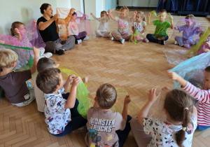 Dzieci biorą udział w rytmicznych zabawach z wykorzystaniem kolorowych chusteczek.